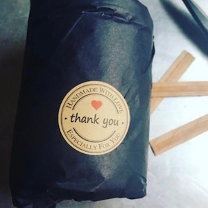 A candle jar wrapped in black tissue paper with a circular Kraft   paper sticker.  Next to the wrapped candle