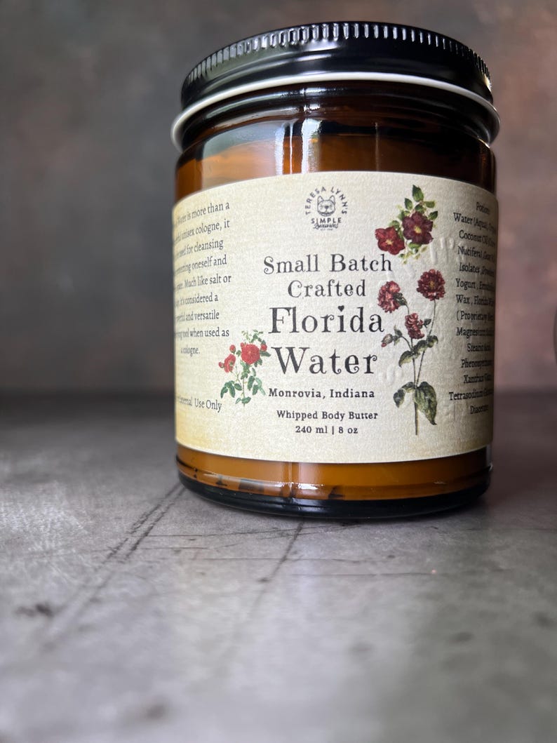 Pode incluir: Um frasco de vidro &acirc;mbar com tampa preta contendo manteiga corporal batida. O r&oacute;tulo diz Small Batch Crafted Florida Water, Monrovia, Indiana, e 240 ml, com ilustra&ccedil;&otilde;es bot&acirc;nicas de flores vermelhas e folhas verdes num fundo creme.