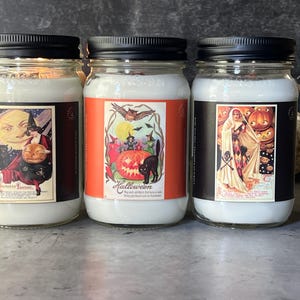 May include: Three glass mason jars filled with white wax and topped with black lids. Each jar features a rectangular label with vintage-style Halloween illustrations, including a witch, a black cat, a jack-o'-lantern, and a costumed figure.