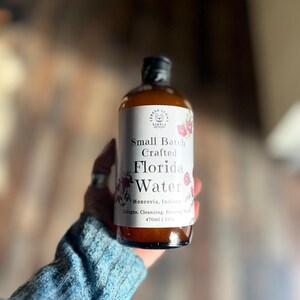 Pode incluir: Uma garrafa de vidro castanho de Teresa Lynn's Simple Scents Small Batch Crafted Florida Water. O r&oacute;tulo branco apresenta ilustra&ccedil;&otilde;es florais, o texto Monrovia, Indiana, e o volume 470ml | 16oz. Est&aacute; rotulado como Cologne, Cleansing, Blessing Water.
