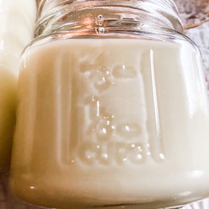 A mason jar with measuring increments filled with a sand colored candle.