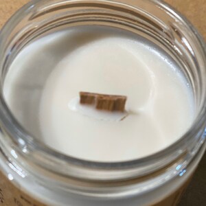 May include: Close-up of a white candle with a wooden wick in a clear glass jar.