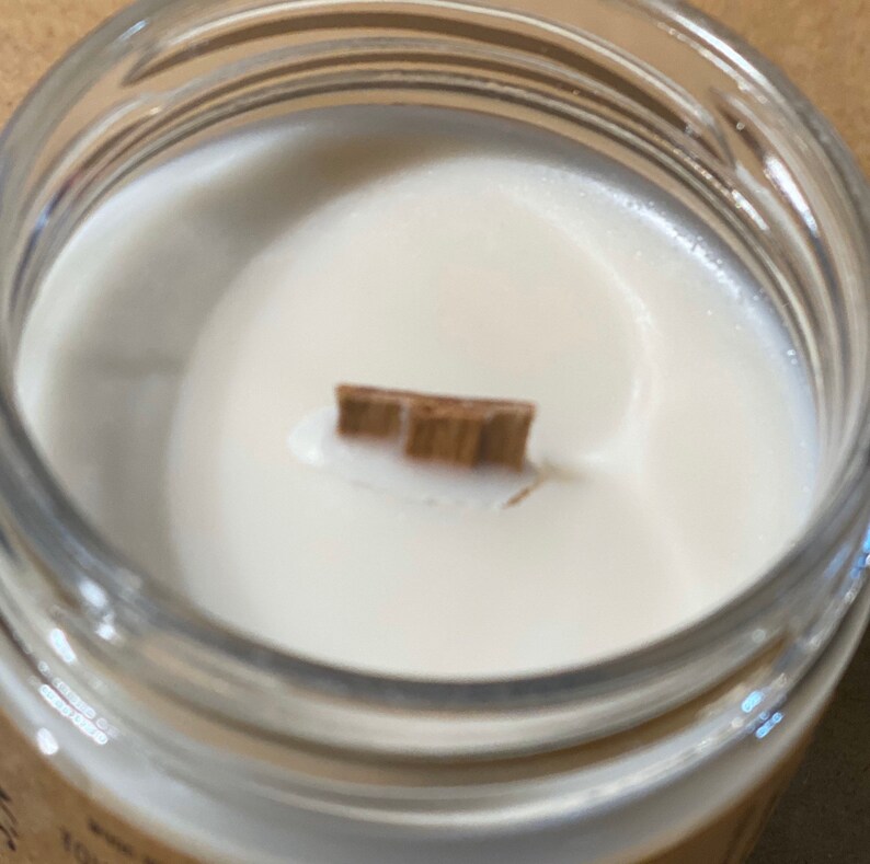 May include: Close-up of a white candle with a wooden wick in a clear glass jar.