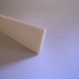 May include: A close-up of a light-colored, unfinished wooden plank. The wood grain is visible, and the plank has a rectangular shape. The end of the plank is visible, showing the layered wood.