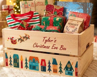 May include: A light-colored wooden crate with the text Tyler's Christmas Eve Box, featuring a Santa sleigh graphic and a colorful village illustration. The crate is filled with wrapped gifts, a striped shirt, and a bag labeled Reindeer Food.