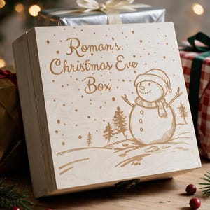 May include: A square light-coloured wooden box with a hinged lid featuring an engraved snowman, pine trees, and the text Roman's Christmas Eve Box. The box has a small metal latch on the front and is decorated with a festive winter scene design.
