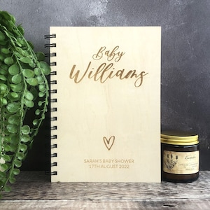 May include: A wooden journal with a gold inscription that reads "Baby Williams, Sarah's Baby Shower, 17th August 2022". A heart symbol is above the date.
