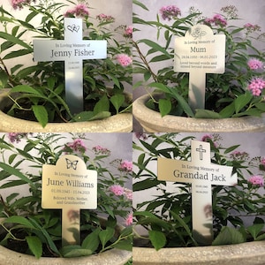 May include: Four silver and gold metal grave markers with crosses and butterflies. The markers have engraved text including names, dates, and messages like "In Loving Memory of" and "Beloved Wife, Mother, and Grandmother".