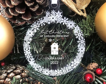 May include: Clear glass Christmas bauble with a white snowflake design. The bauble has the text "First Christmas at 14 Ellen Crescent Louisa & Gary 2022" printed on it.