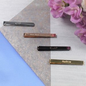 May include: Four personalised tie bars, one silver, one rose gold, one black and one gold. The tie bars are engraved with the names "CTP", "Best Man 20.02.2019", "C.J.P" and "Andrew".