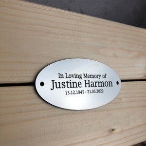 May include: Silver oval memorial plaque with black text that reads "In Loving Memory of Justine Harmon 15.12.1945 - 21.05.2022".