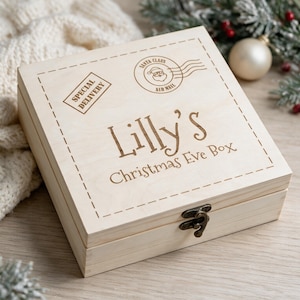 Könnte beinhalten: Eine quadratische, helle Holzbox mit Klappdeckel und Metallverschluss. Der Deckel ist mit einem Lasergravur-Design versehen, das einen gestrichelten Rand, einen Stempel mit SPECIAL DELIVERY, einen Weihnachtsmann-Poststempel und den Text Lilly's Christmas Eve Box zeigt.