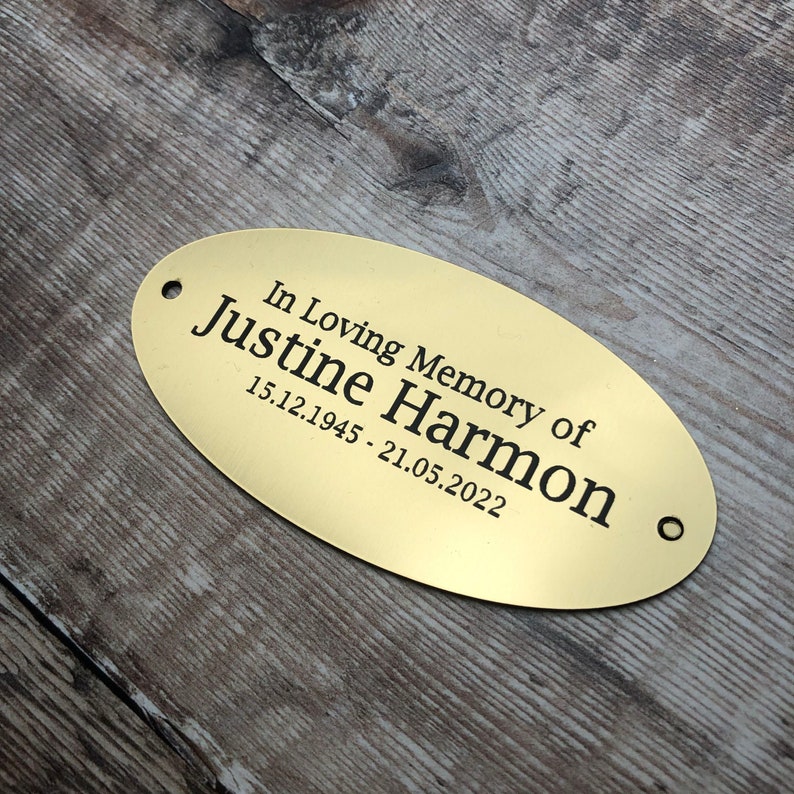 May include: Oval-shaped brass memorial plaque with the text "In Loving Memory of Justine Harmon 15.12.1945 - 21.05.2022".
