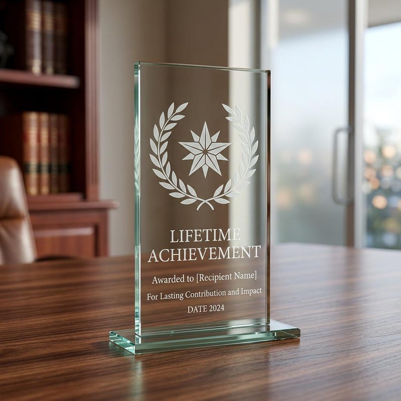 Peut inclure: Un troph&eacute;e en verre transparent avec l'inscription "LIFETIME ACHIEVEMENT". Il pr&eacute;sente une &eacute;toile entour&eacute;e d'une couronne de laurier. Le texte "Awarded to [Recipient Name]" et "DATE 2024" sont &eacute;galement grav&eacute;s.