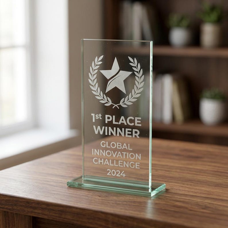 Peut inclure: Troph&eacute;e en verre transparent avec une &eacute;toile et une couronne de laurier. Le texte indique "1st PLACE WINNER GLOBAL INNOVATION CHALLENGE 2024". Le troph&eacute;e rectangulaire est pos&eacute; sur une base rectangulaire, sur une table en bois.