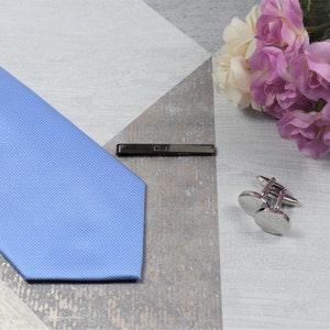 May include: A light blue tie with a tie bar engraved with the initials "C.J.E." and a pair of silver cufflinks.