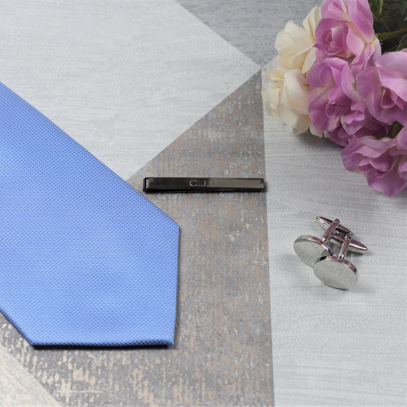 May include: A light blue tie with a tie bar engraved with the initials "C.J.E." and a pair of silver cufflinks.