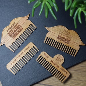 Peut inclure: Quatre peignes &agrave; barbe en bois avec texte grav&eacute; et formes de moustache ou de barbe. Un peigne indique "Robert with great beard comes great responsibility." Un autre dit "Paul I'd love to stay and chat but I really moustache."
