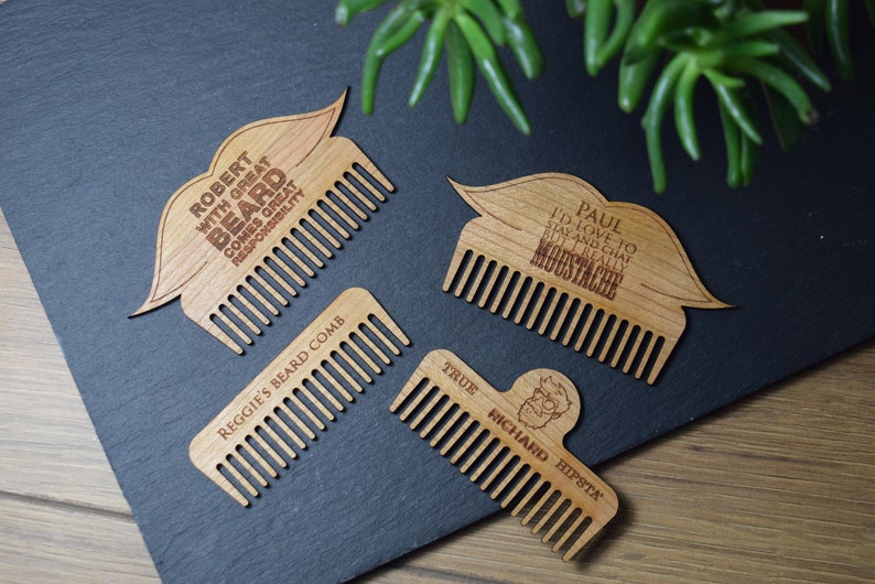 Peut inclure: Quatre peignes &agrave; barbe en bois avec texte grav&eacute; et formes de moustache ou de barbe. Un peigne indique "Robert with great beard comes great responsibility." Un autre dit "Paul I'd love to stay and chat but I really moustache."