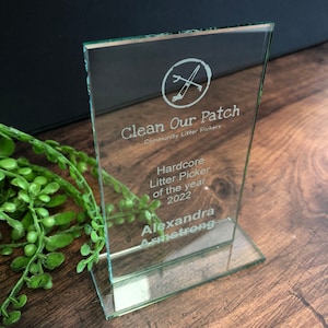 Peut inclure: Un prix en verre transparent avec le texte "Clean Our Patch" et "Hardcore Litter Picker of the year 2022". Le prix a une forme rectangulaire et une base transparente. Le nom "Alexandra Armstrong" est &eacute;galement grav&eacute; sur le prix.