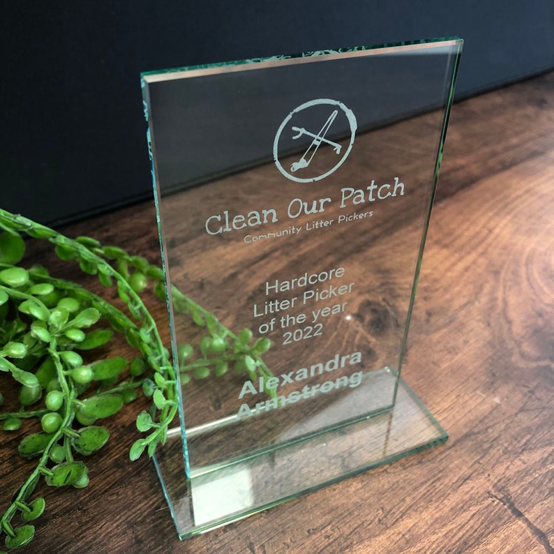 Peut inclure: Un prix en verre transparent avec le texte "Clean Our Patch" et "Hardcore Litter Picker of the year 2022". Le prix a une forme rectangulaire et une base transparente. Le nom "Alexandra Armstrong" est &eacute;galement grav&eacute; sur le prix.
