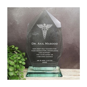 Könnte beinhalten: Eine klare Glasauszeichnung mit grünem Sockel. Die Auszeichnung zeigt ein medizinisches Symbol und den Text "DR. AKIL MASOOD" und "OUR DEEP FELT THANKS FOR YOUR DEDICATION, KNOWLEDGE AND SUPPORT. YOU HAVE GIVEN US A SECOND CHANCE MR & MRS CARTER 2022".