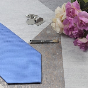 May include: A blue patterned tie, silver cufflinks, and a silver tie bar engraved with the initials "CTP".