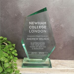 May include: A green glass award plaque with the text "Newham College London" and "Corporation Board Governor Andrew Wilkes" in white. The plaque also includes the text "In appreciation for your many years of service & dedication 2010-2022".