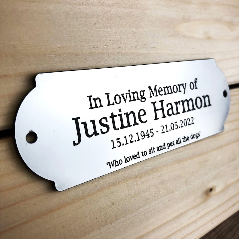 May include: A silver metal plaque with rounded edges and a hole at the top. The plaque reads "In Loving Memory of Justine Harmon 15.12.1945 - 21.05.2022 'Who loved to sit and pet all the dogs'".