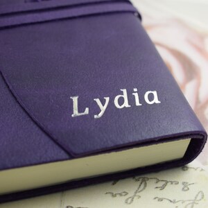 May include: A purple leather-bound journal with the name "Lydia" embossed in silver lettering.
