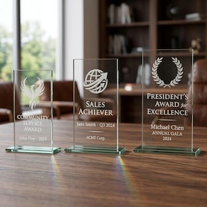 Peut inclure: Trois r&eacute;compenses en verre transparent avec des textes et des motifs grav&eacute;s. L'une indique "Community Service Award", une autre "Sales Achiever" et la troisi&egrave;me "President's Award for Excellence". Chaque r&eacute;compense a une base rectangulaire.