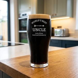 May include: A tall, clear glass filled with dark beer and a foamy head. The glass is etched with the words "WORLD'S BEST UNCLE" above an arrow design, and the text "Lots of love Scott and Jemma xx" below.