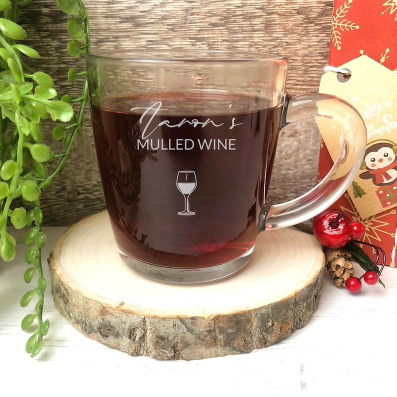 May include: A clear glass mug with a handle, filled with a dark red liquid. The mug has the text "Taron's Mulled Wine" and a white wine glass icon etched on the side.