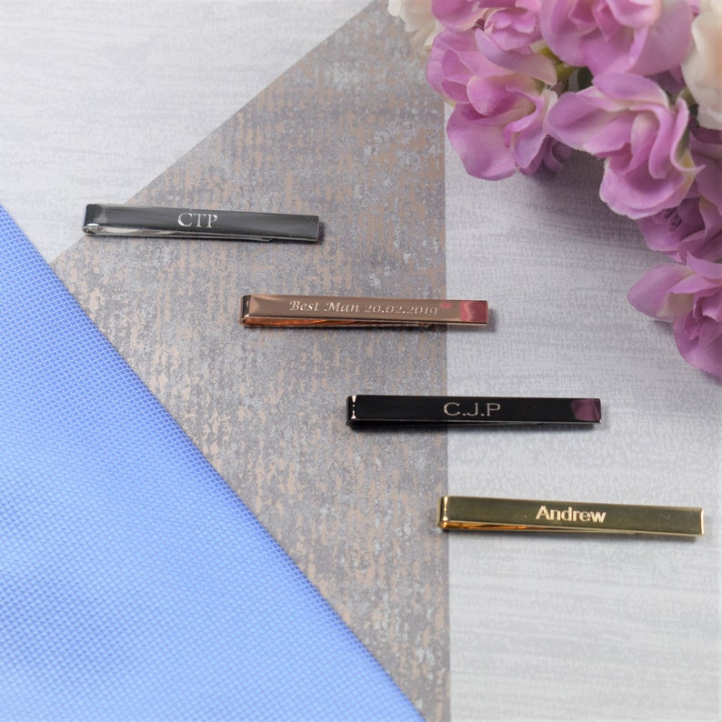 May include: Four personalised tie bars, one silver, one rose gold, one black and one gold. The tie bars are engraved with the names "CTP", "Best Man 20.02.2019", "C.J.P" and "Andrew".