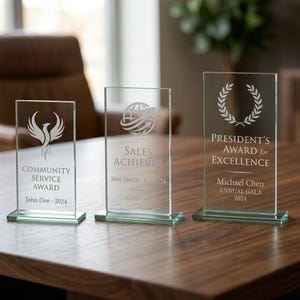 Peut inclure: Trois r&eacute;compenses en verre transparent avec texte et motifs grav&eacute;s. L'une indique &laquo; Community Service Award &raquo; avec un symbole de ph&eacute;nix, une autre &laquo; Sales Achiever &raquo; et la troisi&egrave;me &laquo; President's Award for Excellence &raquo;.