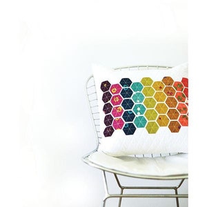 May include: A white pillow with a colorful geometric pattern of hexagons in shades of pink, yellow, green, and blue. The pillow is sitting on a white chair with a silver metal frame. The text "HEXIE PILLOW" and "MODERN HANDCRAFT" is printed below the pillow.