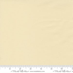 May include: A piece of fabric in a pale yellow color. The fabric has a subtle texture and is marked with a ruler along the bottom edge. The ruler is marked in inches. The brand name "moda" is printed on the ruler.