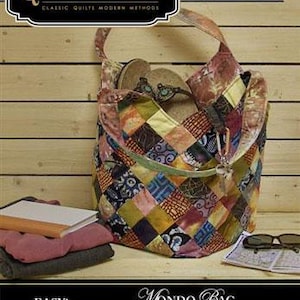 May include: A patchwork Mondo bag, filled with sandals, sits on a wooden surface. The bag features a variety of colorful fabric squares. The image also shows a stack of folded clothes, a pair of sunglasses, and a notebook. The text on the bag says "Quiltsmart".