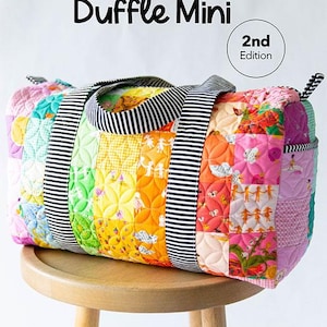 May include: A mini duffle bag featuring a colorful patchwork design with quilted floral and character patterns. The bag has black and white striped handles and includes the text Patchwork Duffle Mini 2nd Edition and Knot + Thread design.