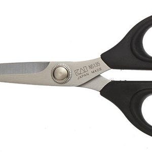 May include: Scissors with black handles and silver blades. The scissors have a rounded design with a central pivot point and the text "KAI N6135 JAPAN MADE" printed on the blade.