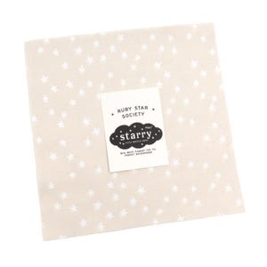 May include: A square, beige fabric with a repeating pattern of white stars. A white label with the text "RUBY STAR SOCIETY" and "starry." is attached. The label also includes the text "WITH WHITE PIGMENT FOR THE PERFECT BACKGROUND!"