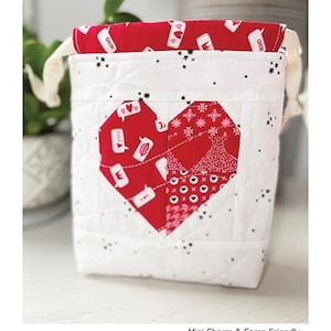 May include: A white drawstring bag with a red heart-shaped patchwork design. The bag is 6 inches by 6 inches by 2 inches. The bag is made by Chrissy Lux of Branch & Blume.