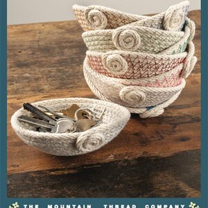 May include: A stack of small, off-white rope bowls with coiled rope accents and colorful zigzag stitching in blue, green, and red. One bowl sits in front containing metal keys and a small fabric tag labeled The Mountain Thread Company.