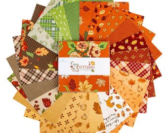 May include: A stack of square fabric swatches arranged in a circular fan pattern. The fabric features autumn-themed prints including pumpkins, leaves, acorns, and plaid patterns in orange, brown, green, and cream. A white paper band reads Cozy Autumn.