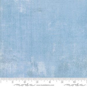 May include: Light blue fabric with a textured, distressed appearance. The fabric has a mottled effect with lighter areas and visible brushstrokes, creating a vintage or rustic aesthetic. The bottom edge features a ruler with inch measurements.