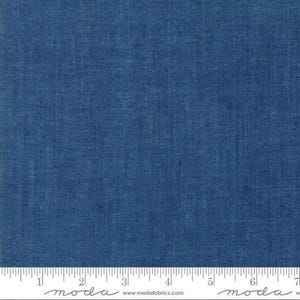 May include: A close-up of a piece of blue fabric with a textured weave. The fabric is a solid, deep blue color. A white ruler with black markings is at the bottom of the image, with the word "moda" printed on it.