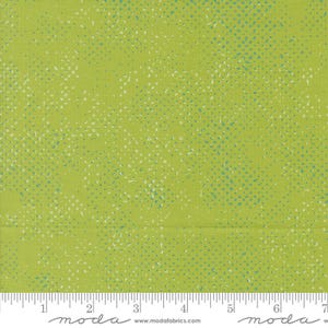 May include: Lime green fabric with a speckled pattern in white and teal. The fabric has a textured appearance and a ruler is visible along the bottom edge, with measurements in inches.
