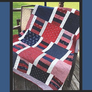 May include: A patchwork quilt with red, white, and blue patterns, draped over a wooden chair. The quilt features various geometric designs and the number "1776" at the top. The quilt is made by Tricia Lynn Maloney, Orphan Quilt Designs.