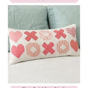 May include: A pink and white patchwork pillow with a heart and X pattern. The pillow is 12 inches by 24 inches and is described as "Sweetheart Pillow".