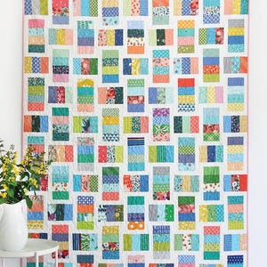 May include: A colorful patchwork quilt with the text "Tick Tock" at the top. The quilt features a grid of rectangular blocks in various colors and patterns. The text "Jelly Roll, Layer Cake, & Scrap friendly!" is also visible.